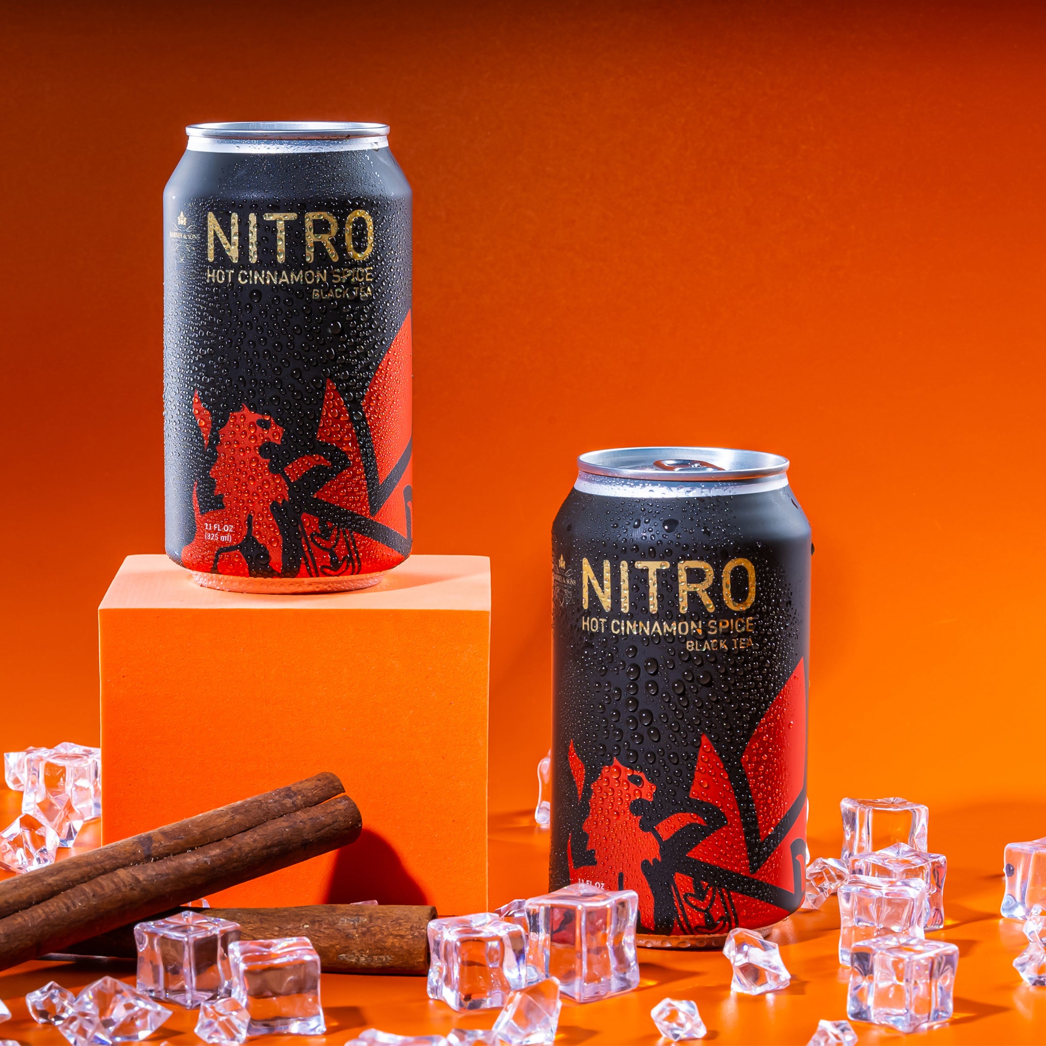 Cans of Hot Cinnamon Spice Nitrogen Tea on an orange background, surrounded by ice and cinnamon sticks.