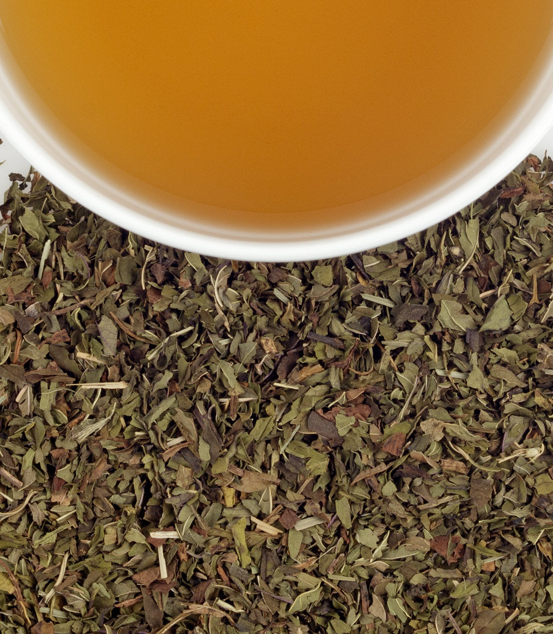 A cup of brewed peppermint herbal tea sits atop dried peppermint leaves, showcasing its natural ingredients.