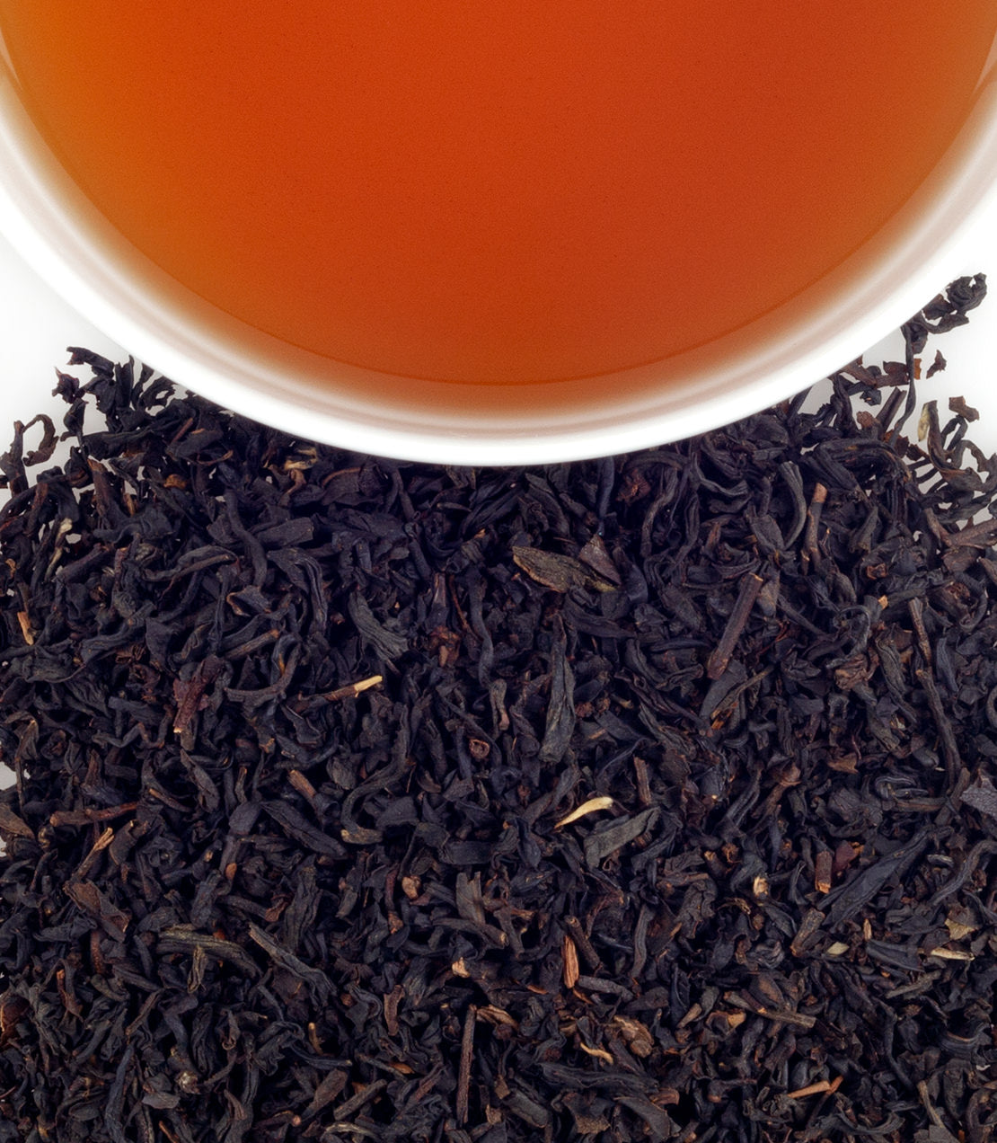 Tower of London Blend tea in a white cup, surrounded by loose black tea leaves on a white background.