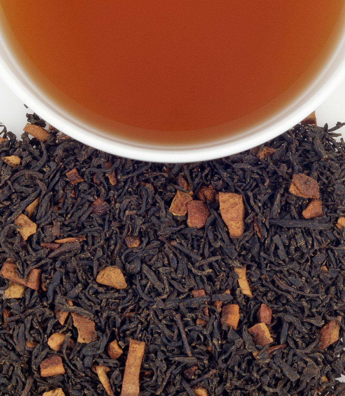 A close-up of loose black tea leaves mixed with cinnamon pieces, alongside a cup of brewed hot cinnamon spice tea.